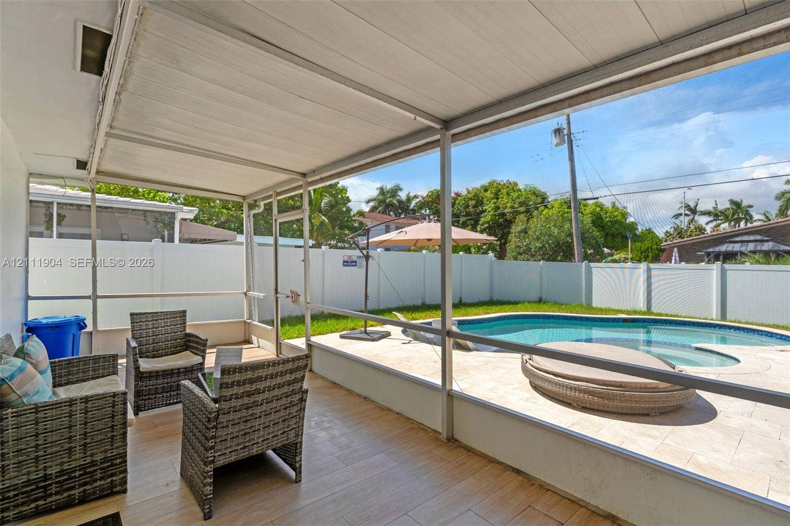 821 Harrison Street, Hollywood, FL 33019 Screened-in lanai featuring wood-finish tile flooring, paved pool deck, custom-shaped swimming pool, and white vinyl privacy fencing