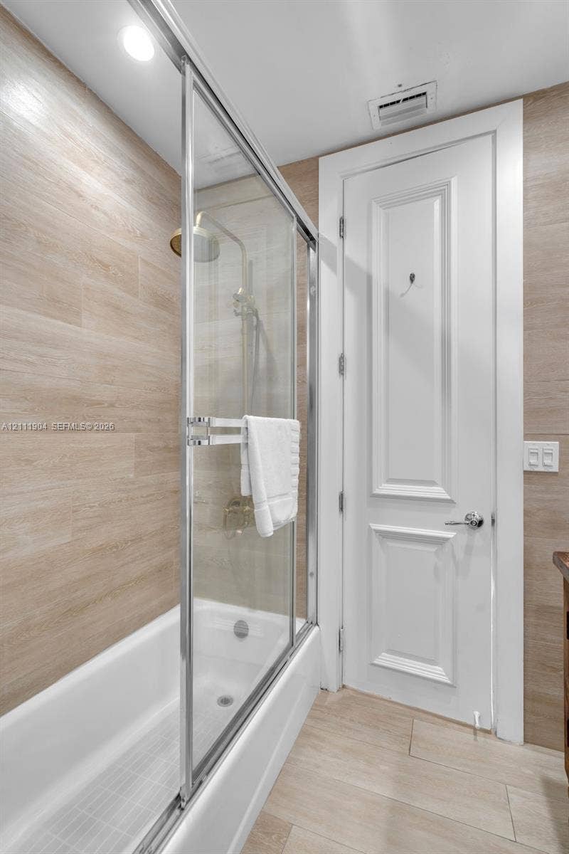 821 Harrison Street, Hollywood, FL 33019 Shower enclosure with sliding glass door, neutral-tone horizontal tile surround, polished metal hardware, and two-panel interior door