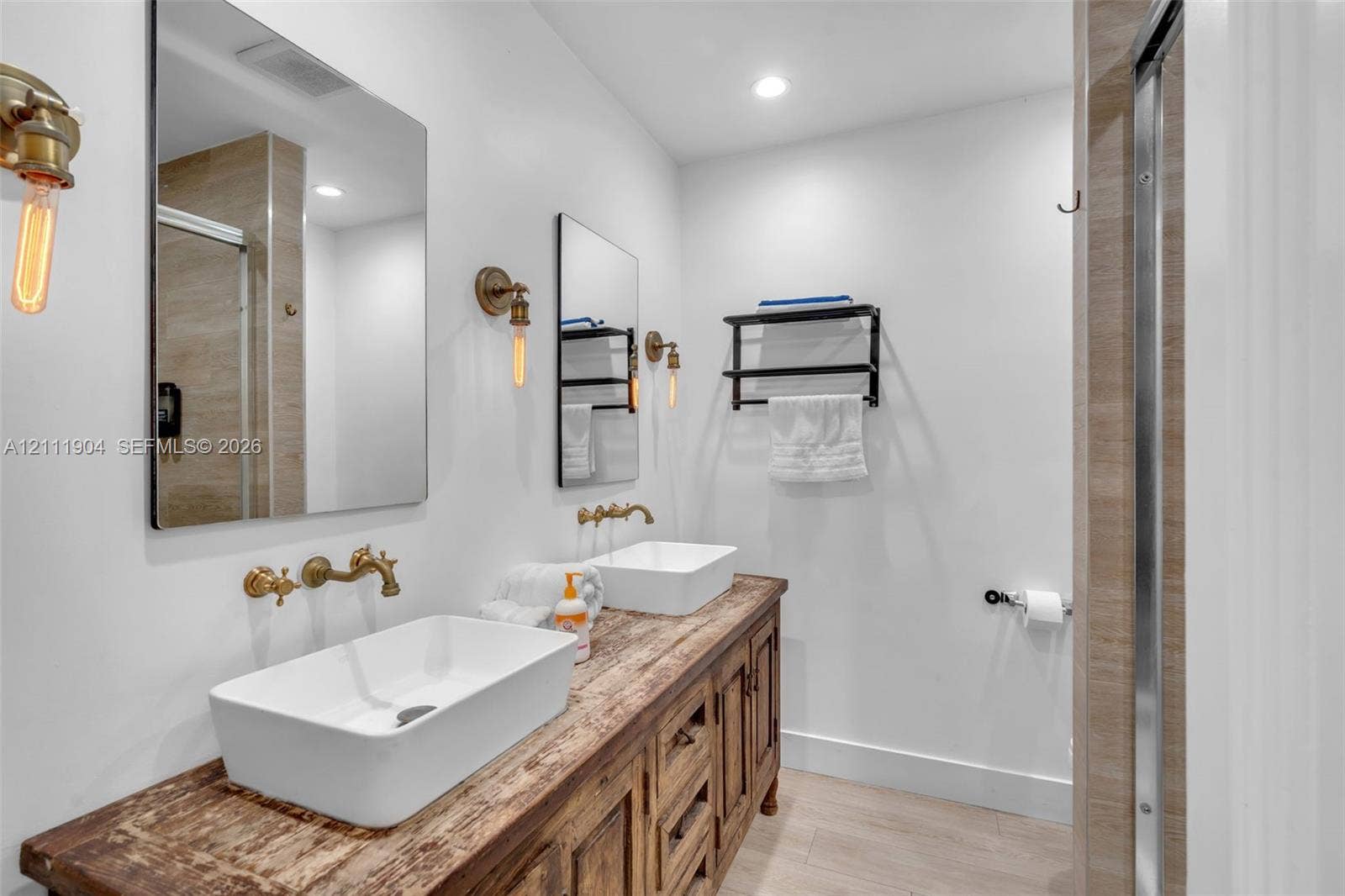 821 Harrison Street, Hollywood, FL 33019 Double vanity featuring a rustic wood-finish cabinet, rectangular vessel sinks, wall-mounted brass faucets, and industrial-style Edison bulb light fixtures