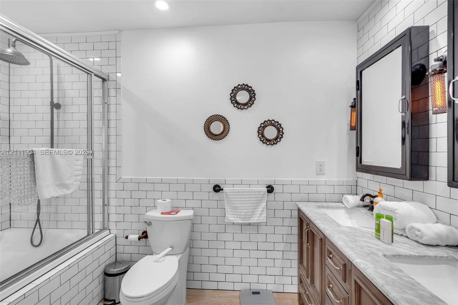 821 Harrison Street, Hollywood, FL 33019 Bathroom featuring white subway tile wall treatments, a dual-sink vanity with light-toned stone-finish countertop, industrial-style wall-mounted medicine cabinets, and a glass-enclosed shower with a rain-style showerhead