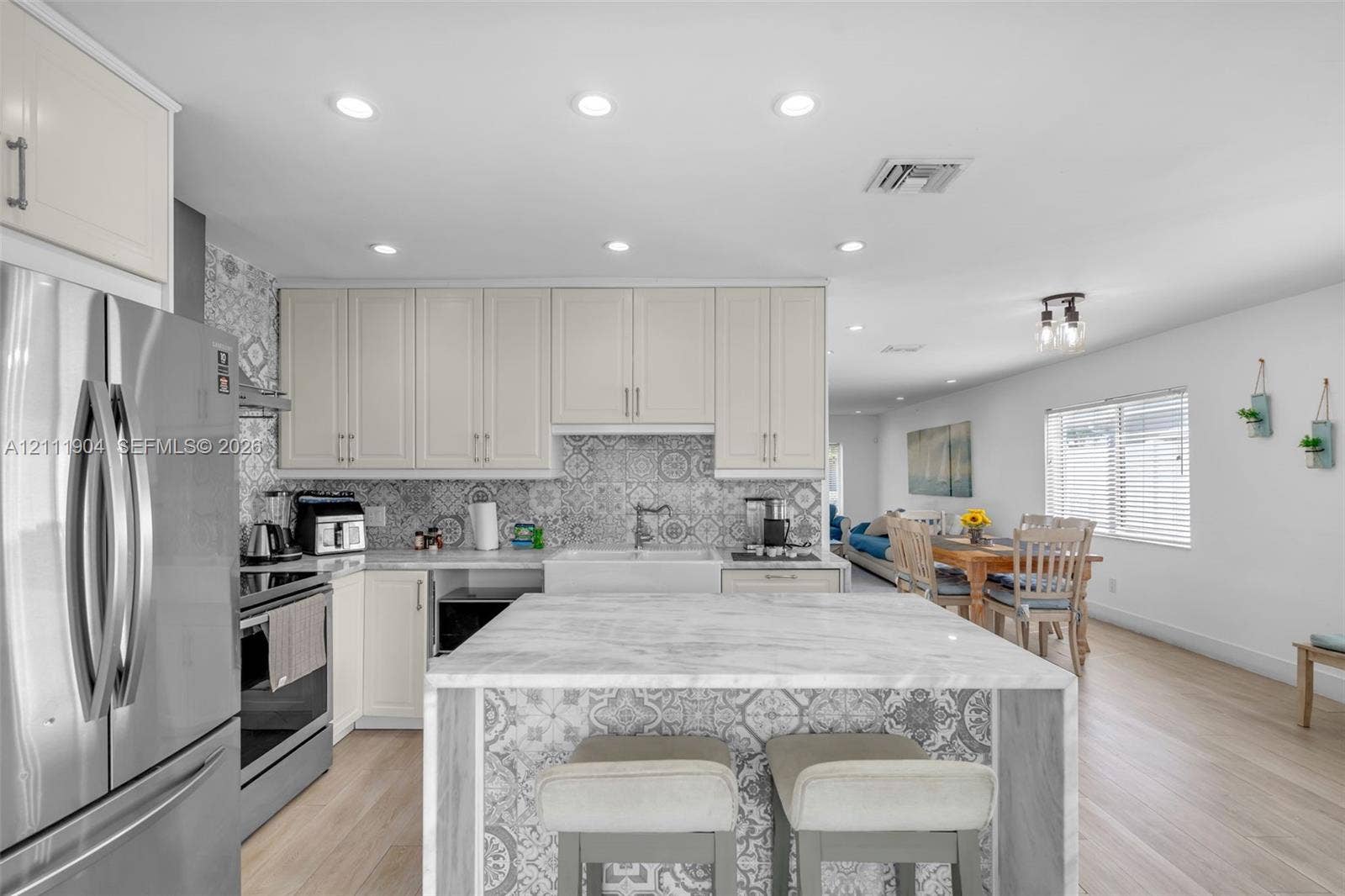 821 Harrison Street, Hollywood, FL 33019 Kitchen featuring light-toned cabinetry, patterned tile backsplash, central island with a stone-finish countertop, stainless steel refrigerator, and wood-finish flooring