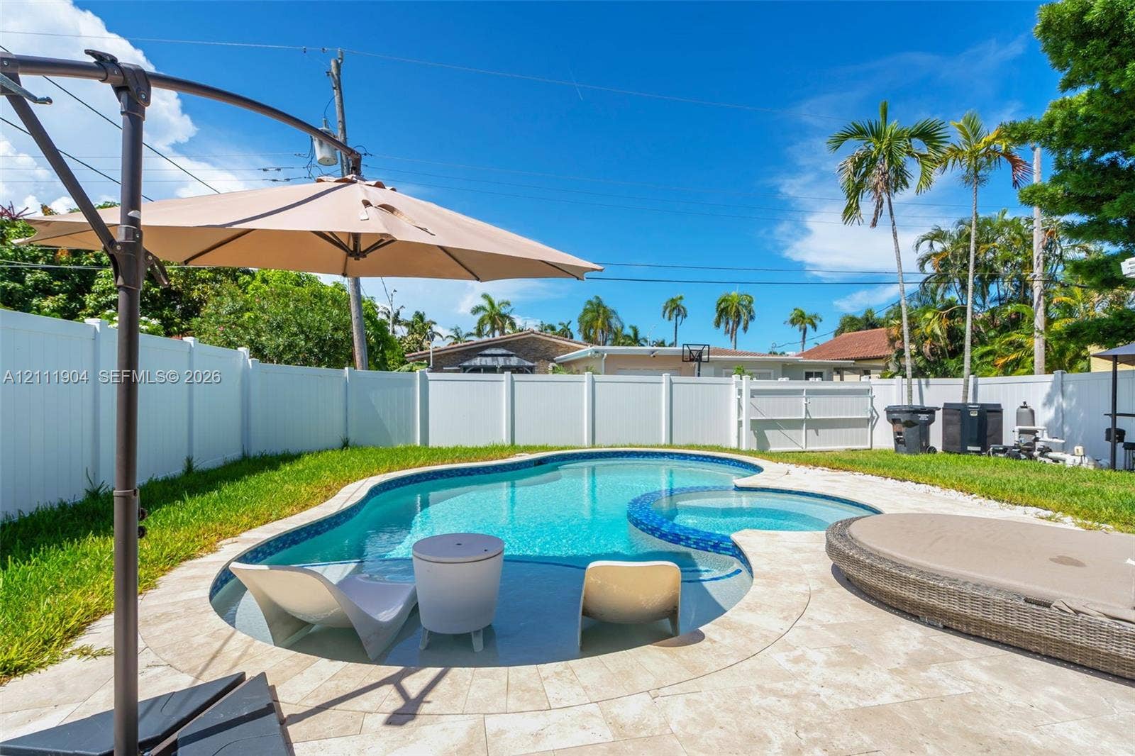 821 Harrison Street, Hollywood, FL 33019 Private backyard featuring an in-ground pool with integrated spa, light-toned stone pool decking, and white vinyl privacy fencing