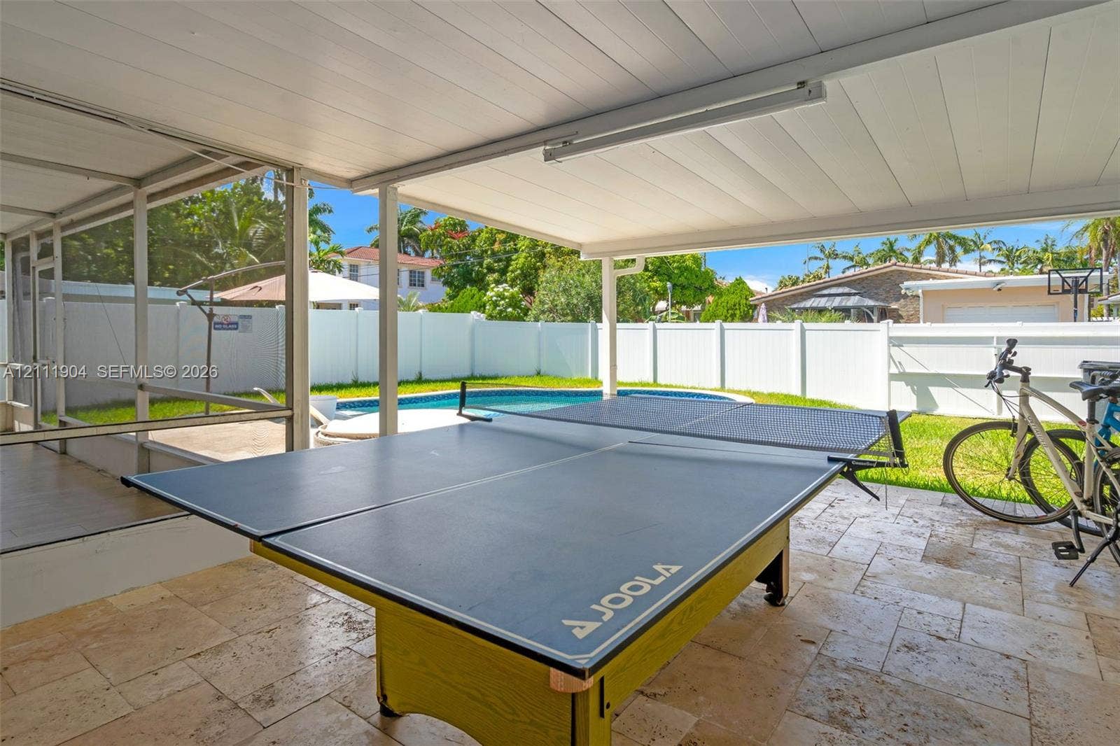 821 Harrison Street, Hollywood, FL 33019 Covered screened-in patio featuring stone-tile flooring and a white vinyl perimeter fence enclosing an outdoor pool