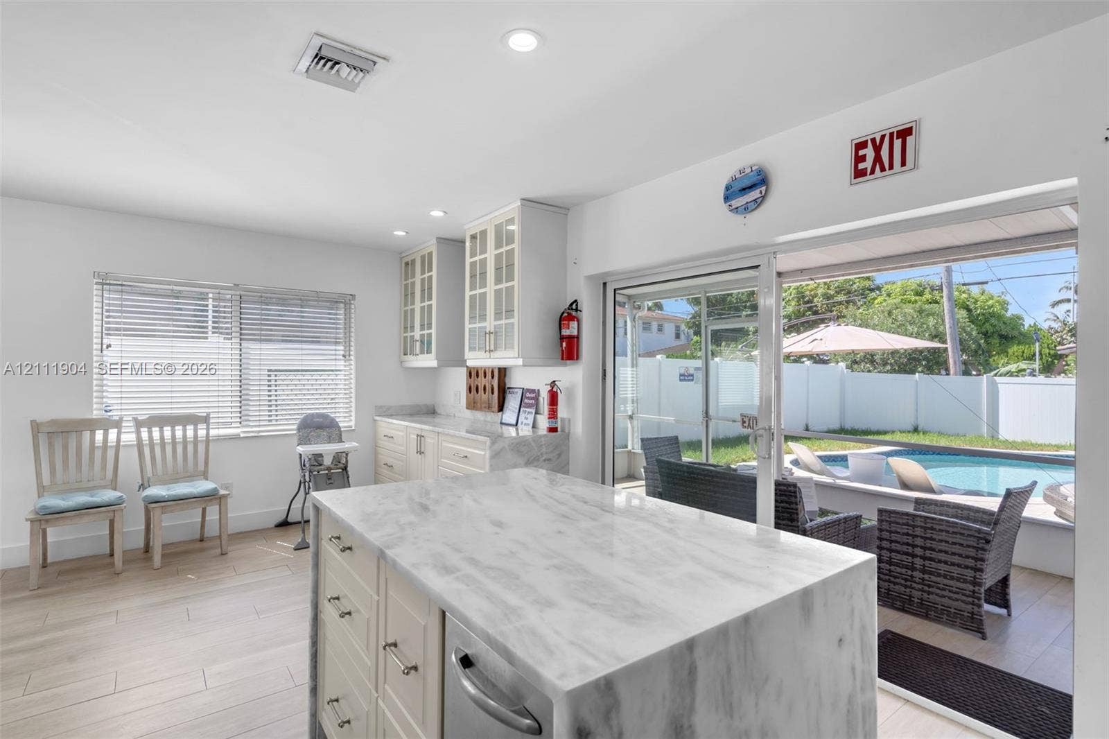821 Harrison Street, Hollywood, FL 33019 Kitchen featuring a stone-topped waterfall island, custom cabinetry with glass-front uppers, wood-finish flooring, recessed lighting, and a sliding glass door providing external access to the pool area