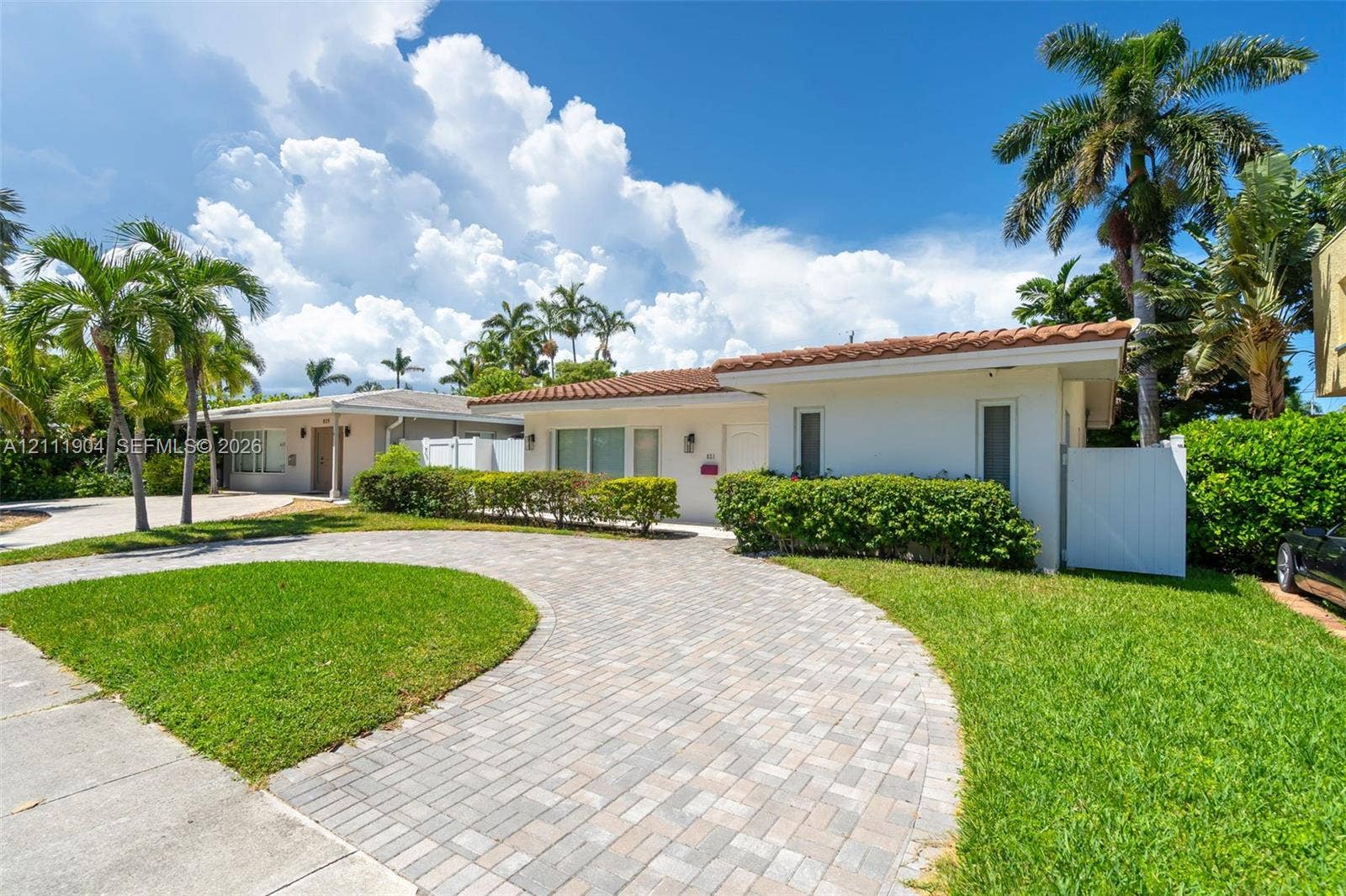 821 Harrison Street, Hollywood, FL 33019 Single-story exterior featuring a clay tile roof, white stucco finish, circular paver driveway, and manicured lawn with mature palm trees