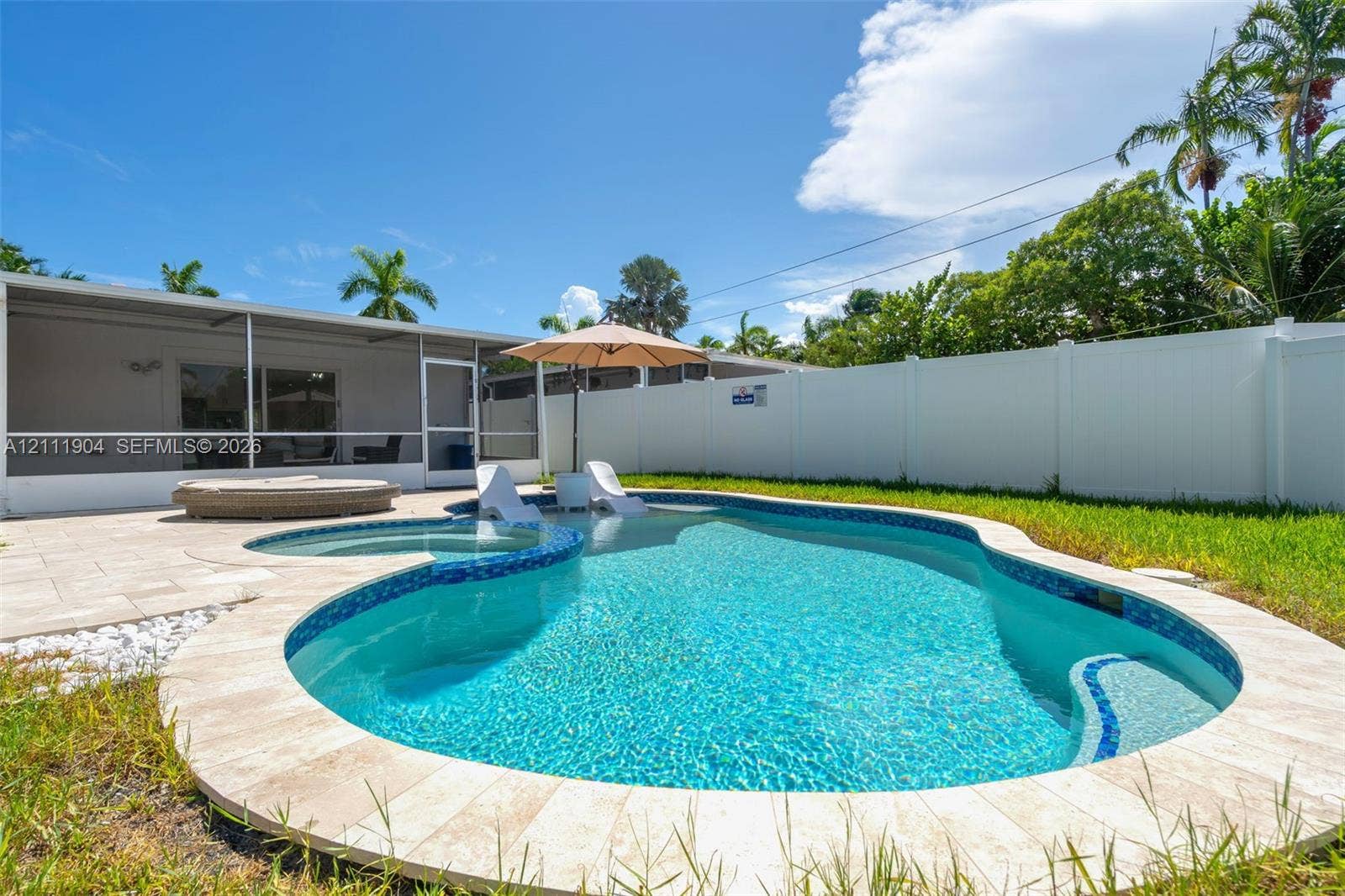 821 Harrison Street, Hollywood, FL 33019 Free-form in-ground swimming pool with an integrated spa, stone-paver decking, screened-in patio, and vinyl privacy fencing