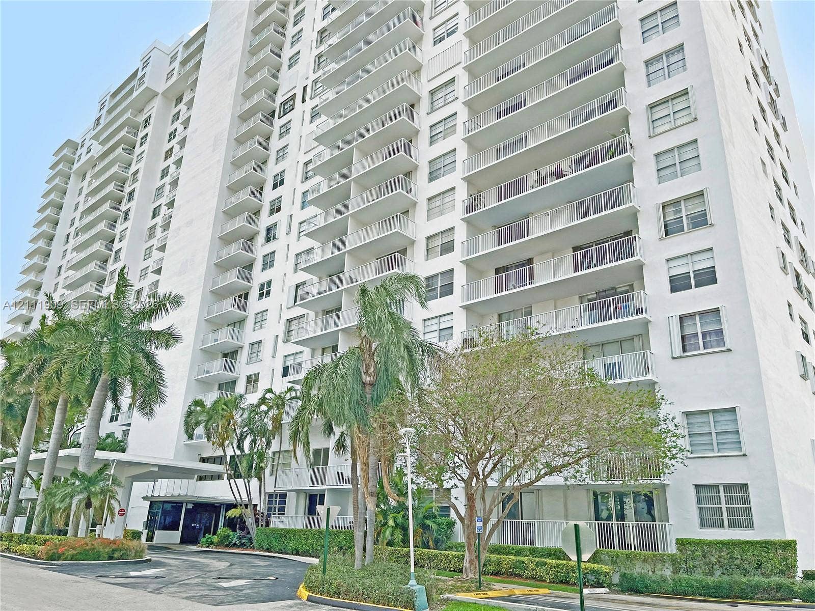 2851 NE 183rd Street, #1708E, Aventura, FL 33160 High-rise multi-story building featuring tiered private balconies, an expansive concrete motor court, a covered entryway portico, and mature tropical landscaping