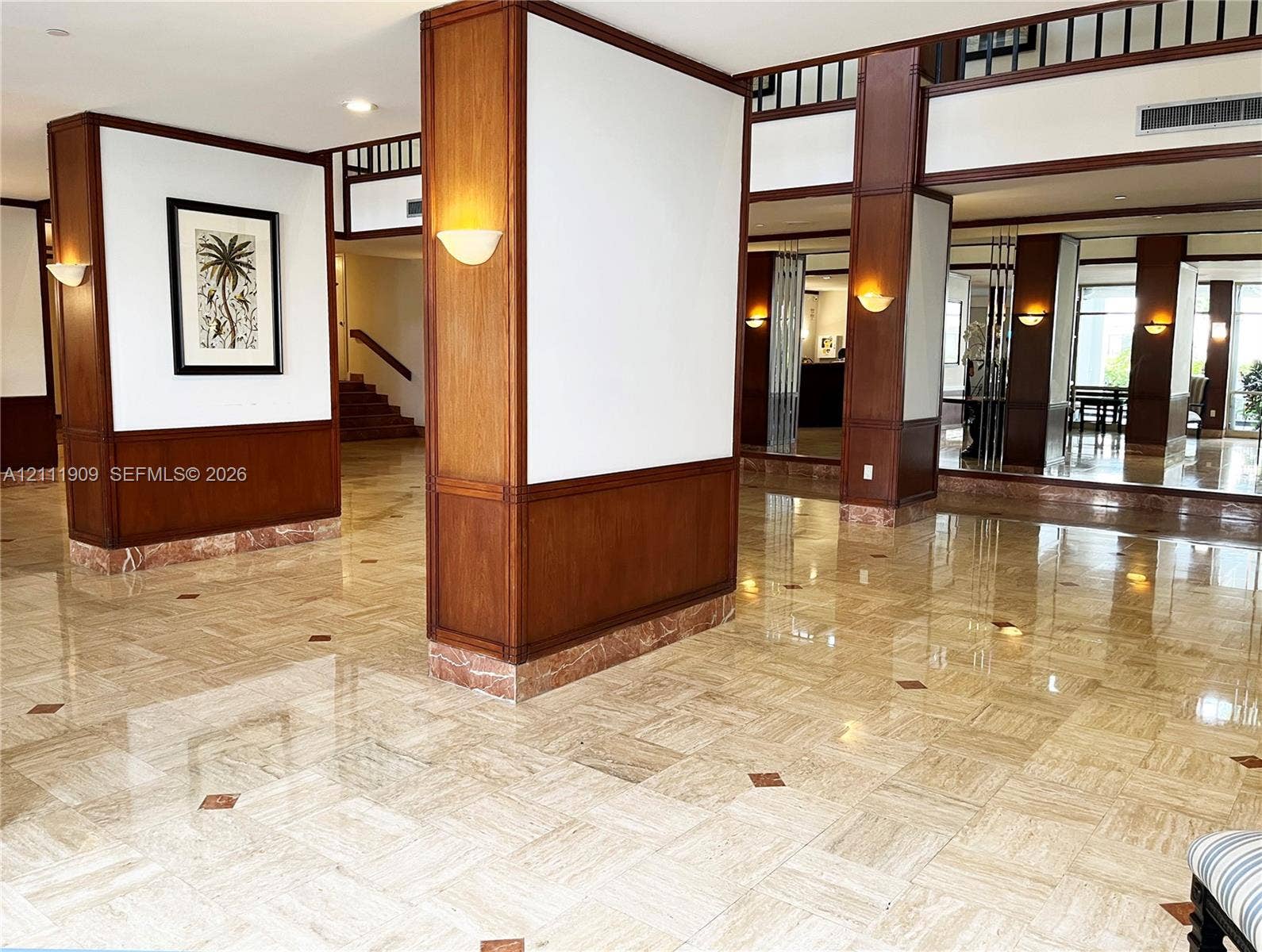 2851 NE 183rd Street, #1708E, Aventura, FL 33160 Polished stone tile flooring with decorative stone inlays, wood-paneled support columns, wall-mounted sconce lighting, and a mezzanine-level wood railing