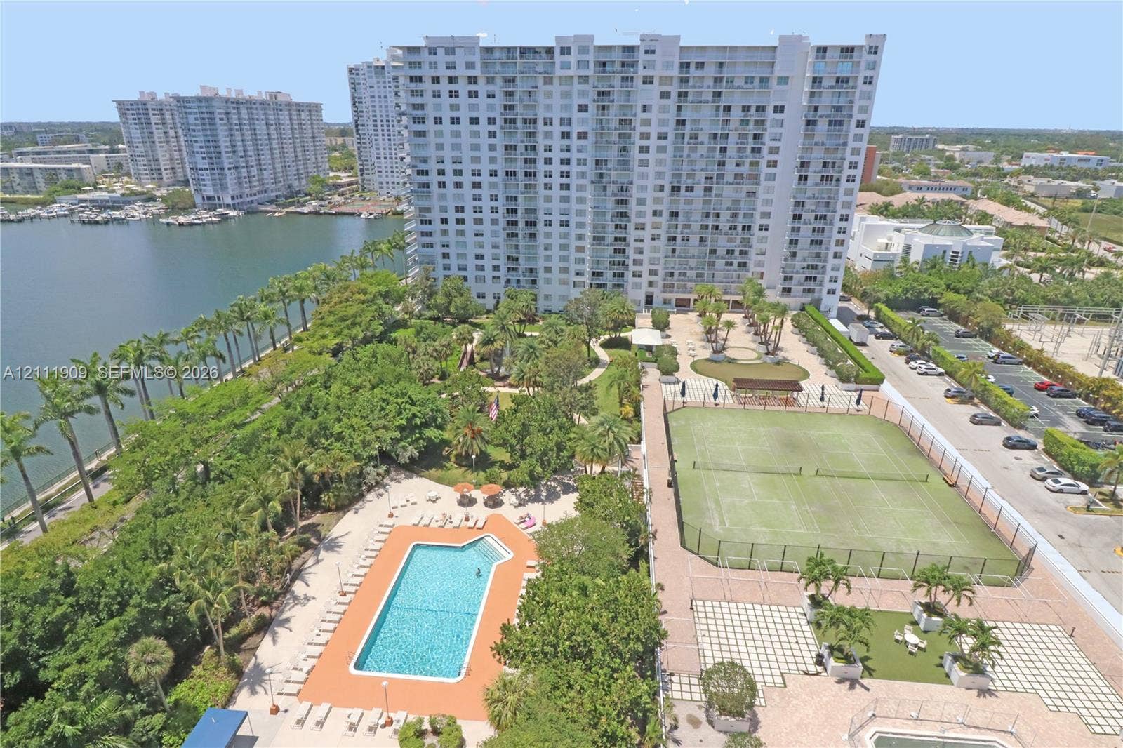 2851 NE 183rd Street, #1708E, Aventura, FL 33160 Aerial perspective of a high-rise residential complex featuring a swimming pool, tennis court, landscaped grounds with mature palm trees, and waterfront access