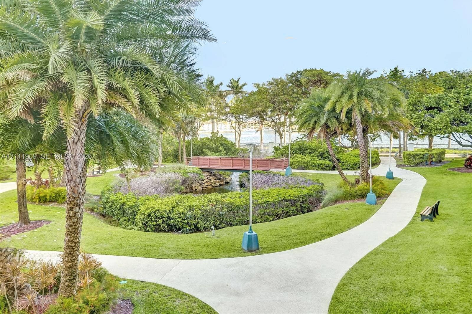 2851 NE 183rd Street, #1708E, Aventura, FL 33160 Landscaped grounds featuring palm trees, a concrete pathway, a decorative wooden bridge, and a water feature