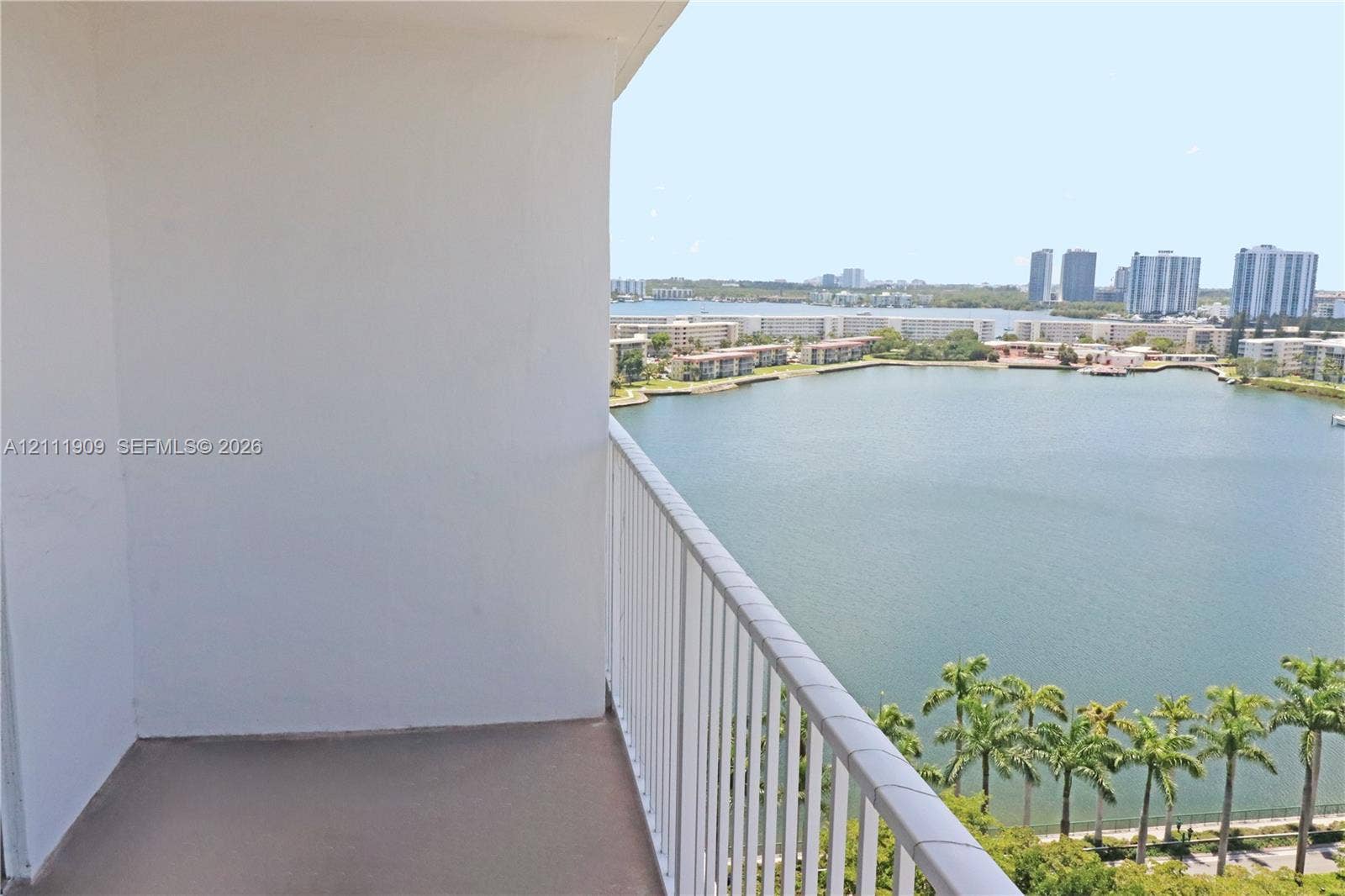 2851 NE 183rd Street, #1708E, Aventura, FL 33160 Covered balcony featuring concrete flooring and a vertical bar metal railing, overlooking an expansive lake and urban skyline
