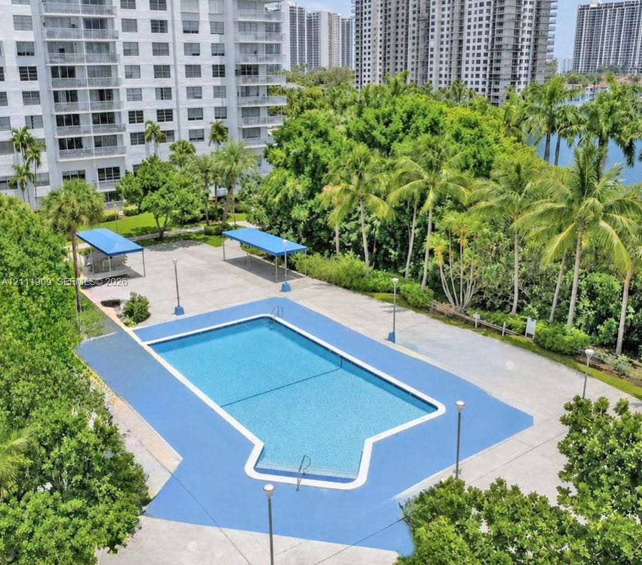 2851 NE 183rd Street, #1708E, Aventura, FL 33160 Outdoor swimming pool featuring a concrete deck, shaded seating areas, pedestal lighting, and lush perimeter landscaping
