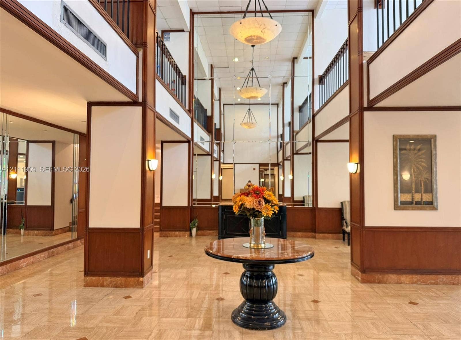 2851 NE 183rd Street, #1708E, Aventura, FL 33160 Multi-story lobby featuring stone flooring, full-height mirrored wall panels, wood-trimmed architectural columns, tiered pendant lighting, and metal balcony railings