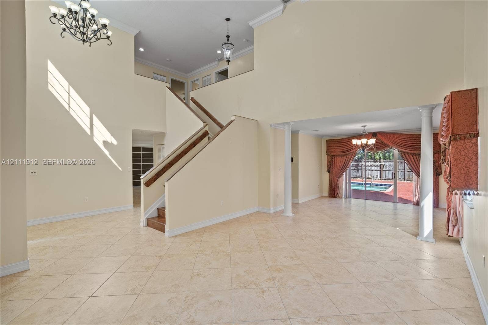 15681 SW 147th Court, Miami, FL 33187 Grand foyer featuring a double-height ceiling, staircase with a wood handrail, decorative chandeliers, tile flooring, and column supports