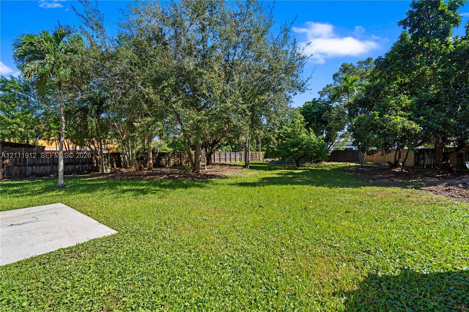 15681 SW 147th Court, Miami, FL 33187 Expansive backyard featuring a concrete patio, mature trees, and wood-panel perimeter fencing