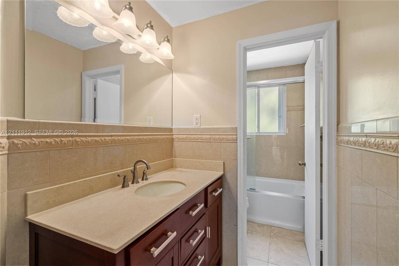 15681 SW 147th Court, Miami, FL 33187 Bathroom featuring a dark wood-finish vanity, stone countertop with an integrated sink, full-width wall mirror, and neutral wall tiling with decorative relief trim