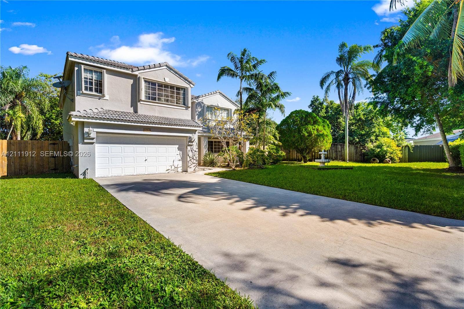 15681 SW 147th Court, Miami, FL 33187 Two-story exterior featuring a light-toned stucco faade, tile roof, multi-car garage, concrete driveway, and expansive lawn with mature palm trees