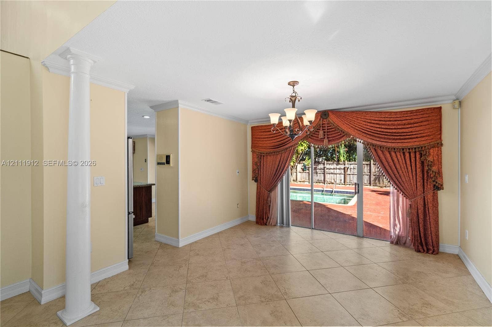 15681 SW 147th Court, Miami, FL 33187 Open-concept room featuring diagonal tile flooring, a decorative structural column, crown molding, a multi-arm chandelier, and sliding glass doors revealing an outdoor pool and patio