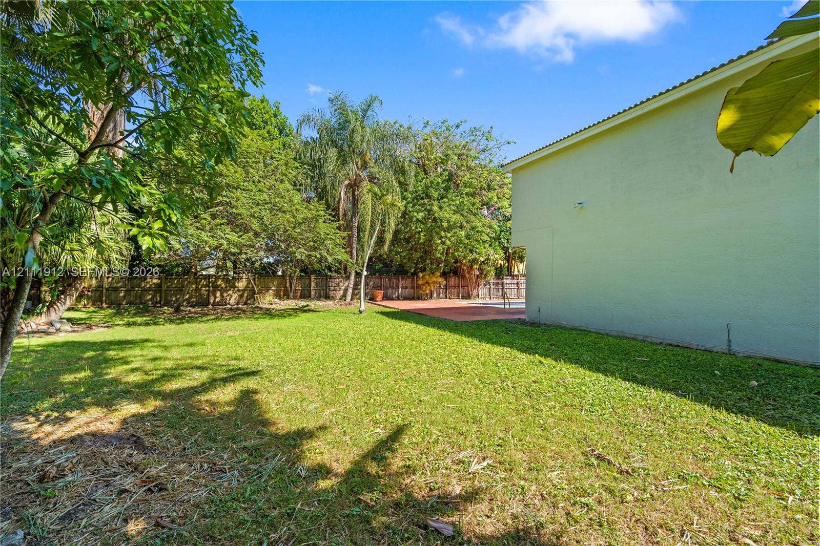 15681 SW 147th Court, Miami, FL 33187 Spacious backyard featuring a large grass lawn, perimeter wood fencing, mature trees, and a paved patio area