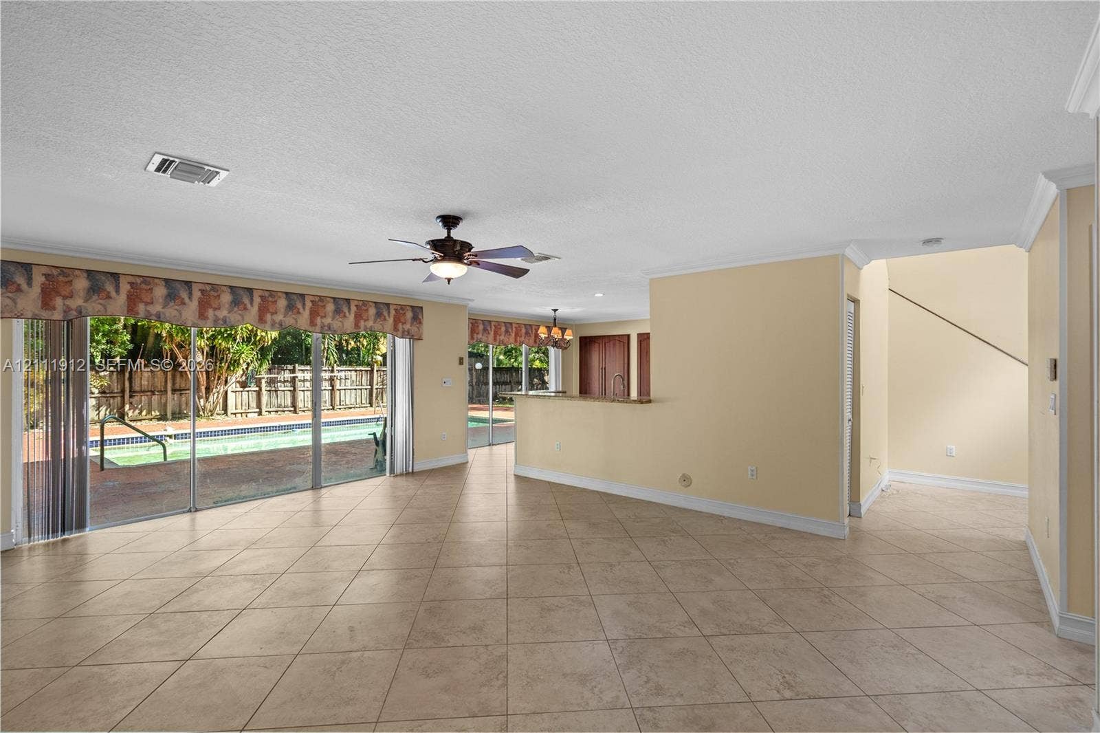 15681 SW 147th Court, Miami, FL 33187 Open-concept interior featuring large-format tile flooring, crown molding, a built-in kitchen peninsula, and sliding glass doors with access to an outdoor pool area
