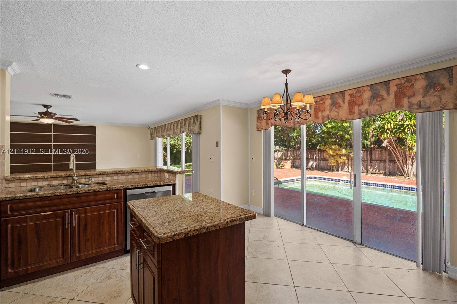 15681 SW 147th Court, Miami, FL 33187 Kitchen featuring wood cabinetry, stone-surface countertops, central island, tile flooring, and sliding glass doors leading to an outdoor pool area