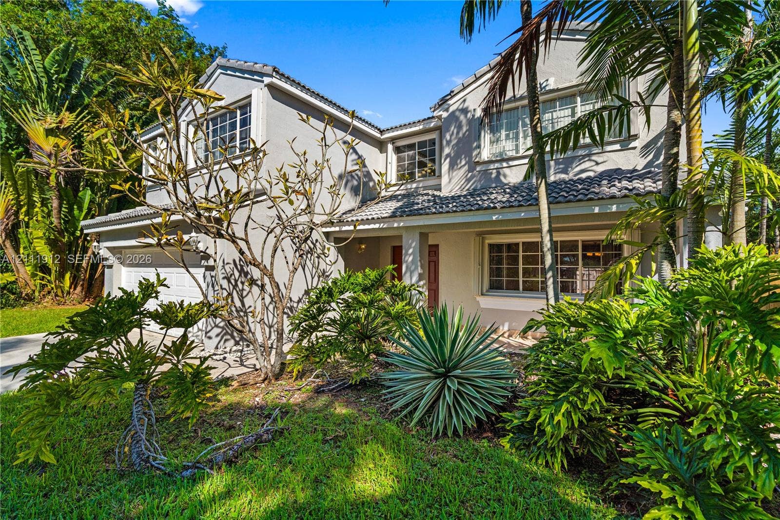 15681 SW 147th Court, Miami, FL 33187 Two-story residence featuring a multi-gabled roofline, light-toned stucco exterior, multi-pane windows, and a paved driveway leading to a multi-car garage
