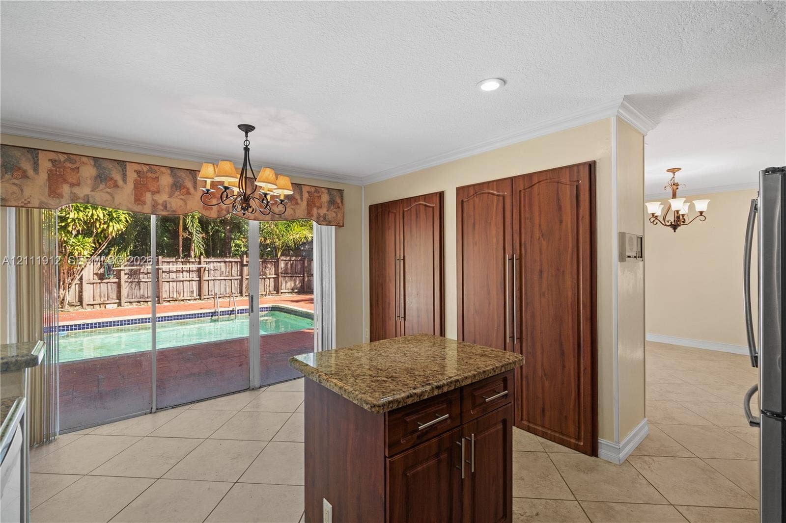 15681 SW 147th Court, Miami, FL 33187 Kitchen featuring a center island with a natural stone countertop, full-height wood cabinetry, neutral tile flooring, and sliding glass doors opening to an exterior swimming pool
