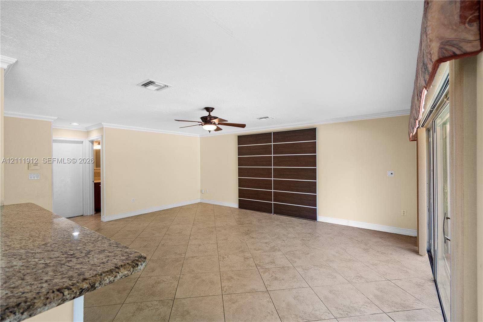 15681 SW 147th Court, Miami, FL 33187 Open-concept interior featuring large-format tile flooring, a stone-surfaced peninsula, a ceiling fan with integrated lighting, and custom dark-toned built-in cabinetry with horizontal detailing