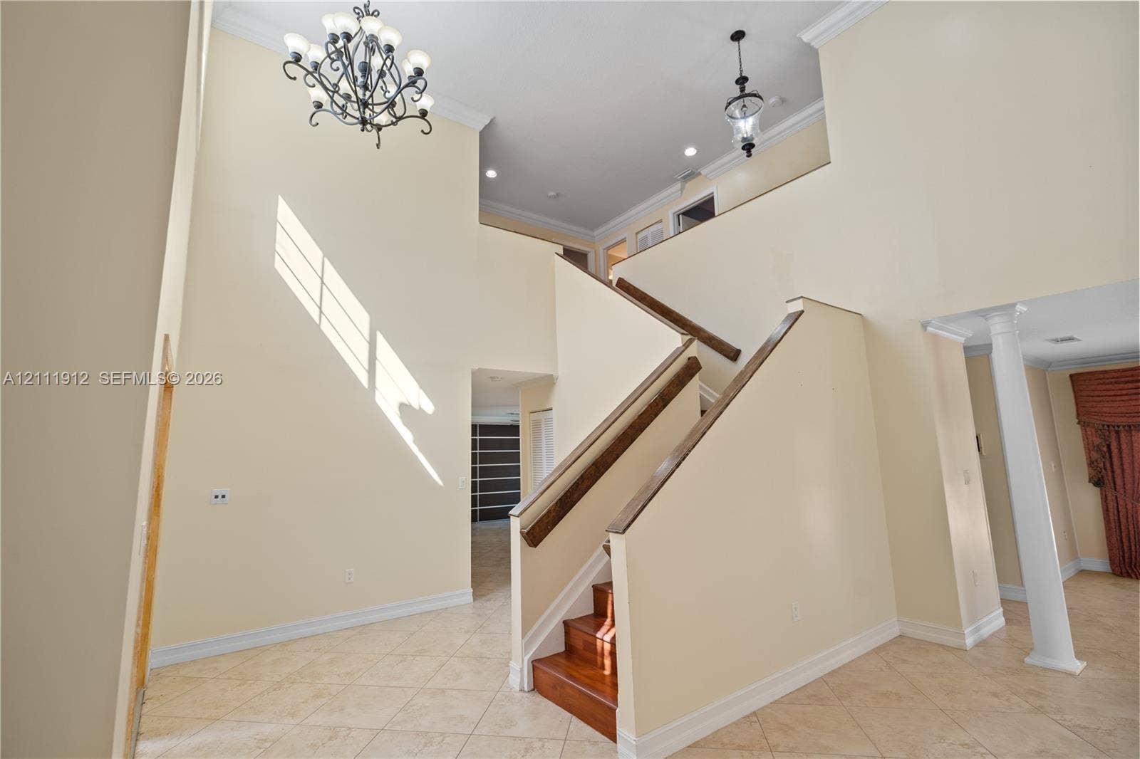 15681 SW 147th Court, Miami, FL 33187 Two-story foyer featuring high ceilings, a decorative wrought-iron chandelier, tile flooring, a prominent staircase with wood treads and handrails, and a structural column