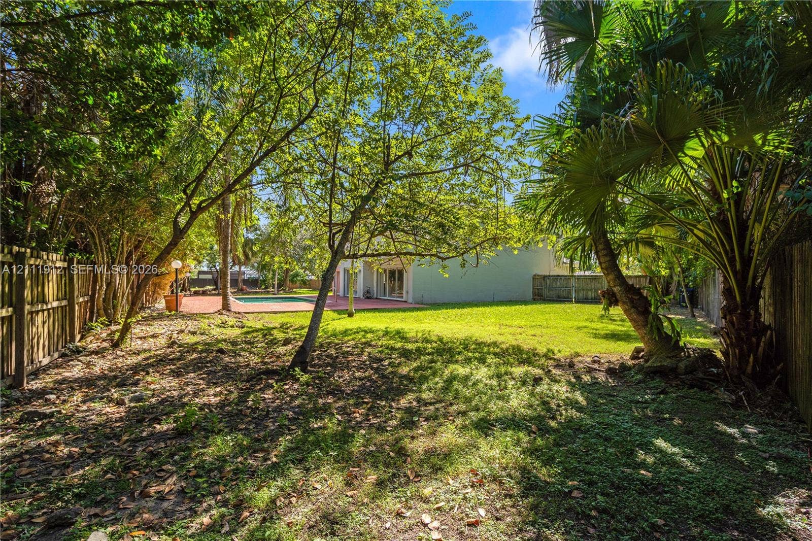 15681 SW 147th Court, Miami, FL 33187 Expansive backyard featuring mature trees, a manicured lawn, a swimming pool, a paved patio area, and wood fencing