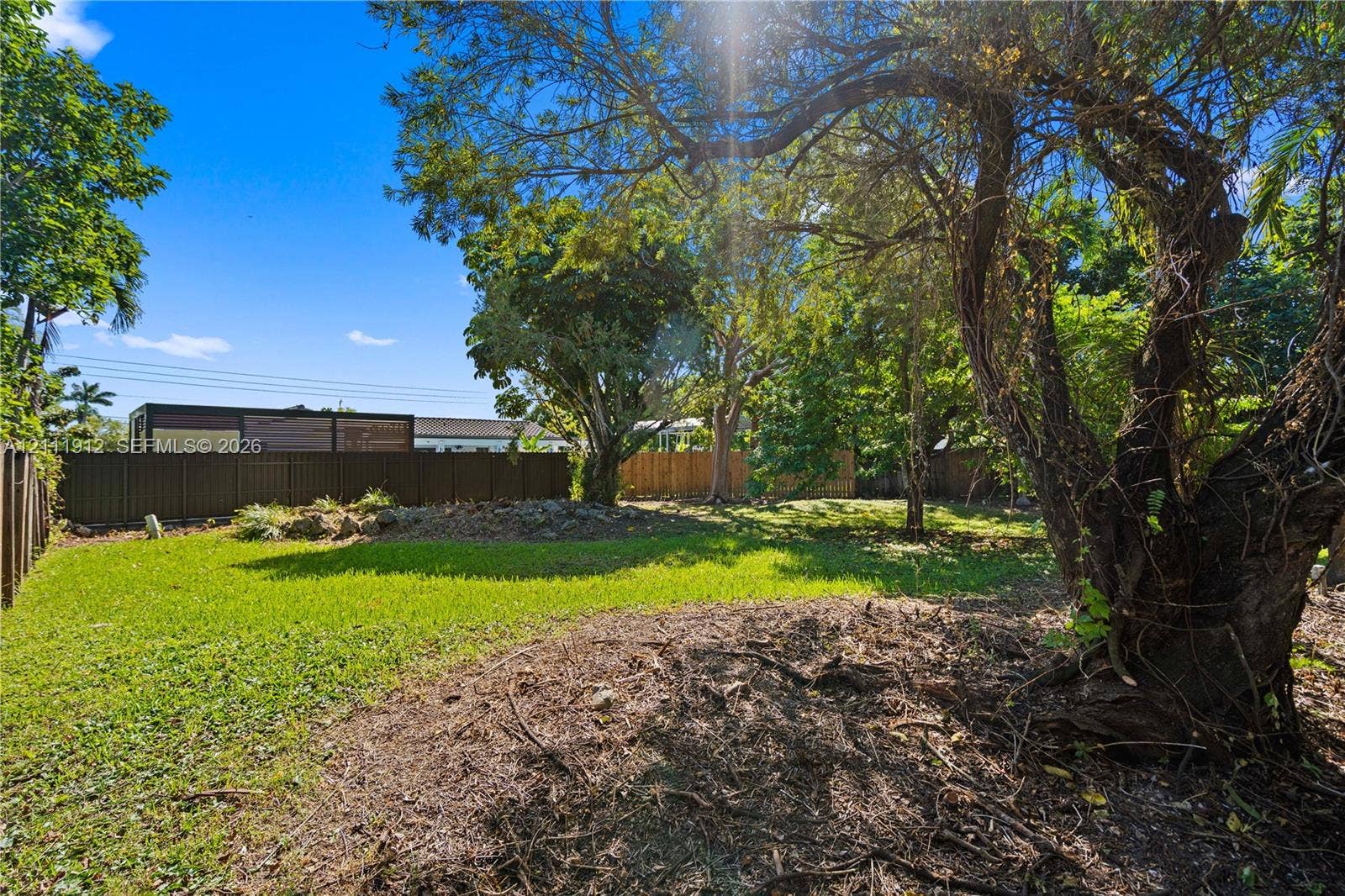 15681 SW 147th Court, Miami, FL 33187 Backyard featuring a manicured lawn, mature trees, and a full-perimeter privacy fence