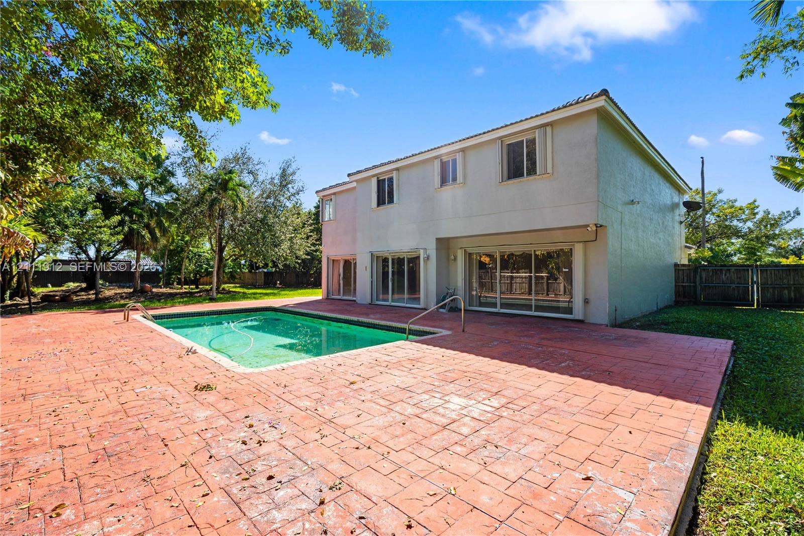 15681 SW 147th Court, Miami, FL 33187 Two-story residence featuring an in-ground swimming pool, expansive stamped concrete patio, sliding glass doors, and mature landscaping