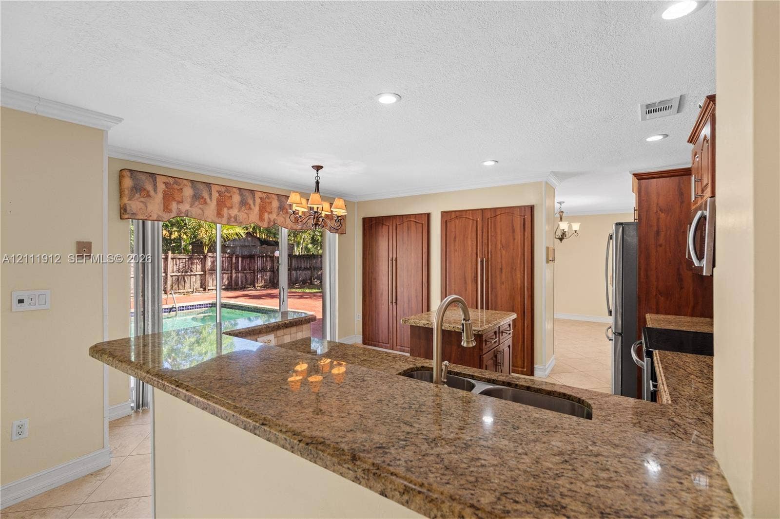 15681 SW 147th Court, Miami, FL 33187 Kitchen featuring a wrap-around stone countertop, recessed lighting, built-in wooden cabinetry, stainless steel sink with gooseneck faucet, and sliding glass doors