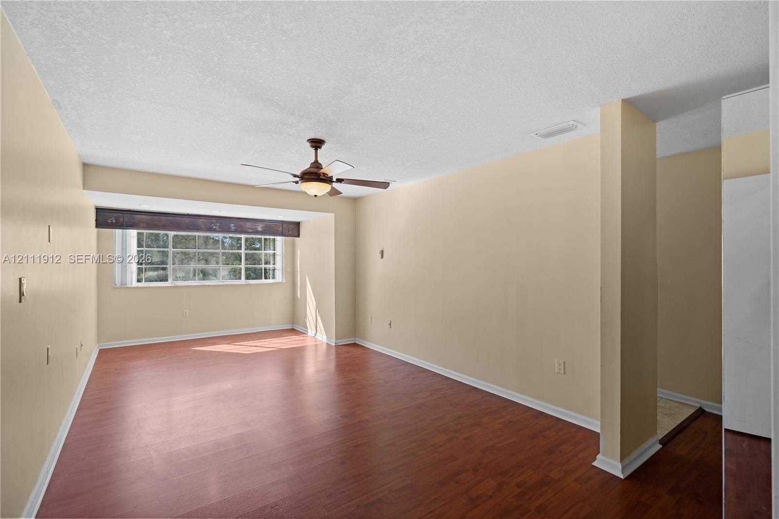 15681 SW 147th Court, Miami, FL 33187 Spacious room featuring wood-finish flooring, a multi-pane window with a valance, and an integrated ceiling fan with a light fixture
