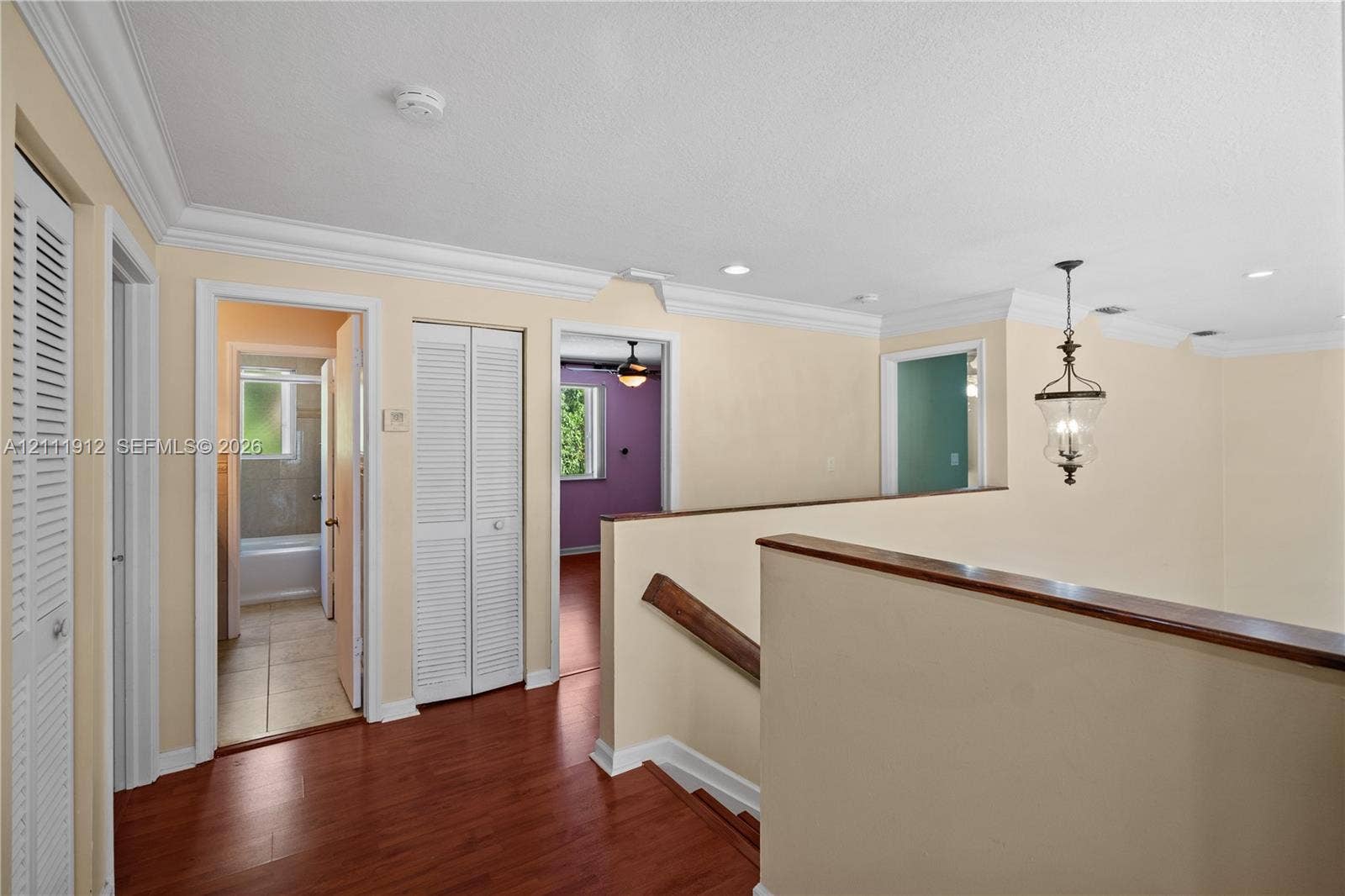 15681 SW 147th Court, Miami, FL 33187 Hallway featuring wood-finish flooring, crown molding, louvered closet doors, and a hanging lantern-style light fixture