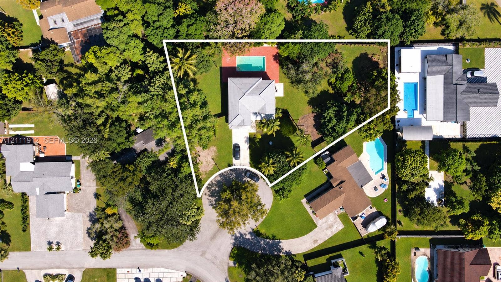 15681 SW 147th Court, Miami, FL 33187 Aerial perspective of a property featuring an in-ground swimming pool, expansive grounds, mature trees, and a paved driveway