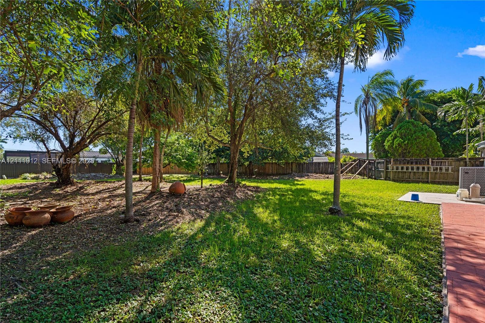 15681 SW 147th Court, Miami, FL 33187 Expansive backyard featuring mature palm trees, established landscaping, perimeter wood fencing, and brick-paver patio surfaces