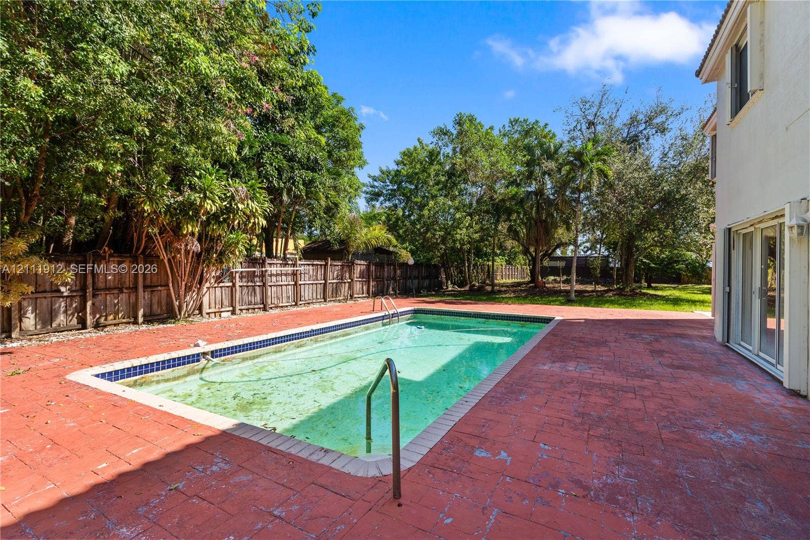 15681 SW 147th Court, Miami, FL 33187 In-ground swimming pool featuring a tiled waterline, surrounded by an expansive paved patio and a wood-slat privacy fence
