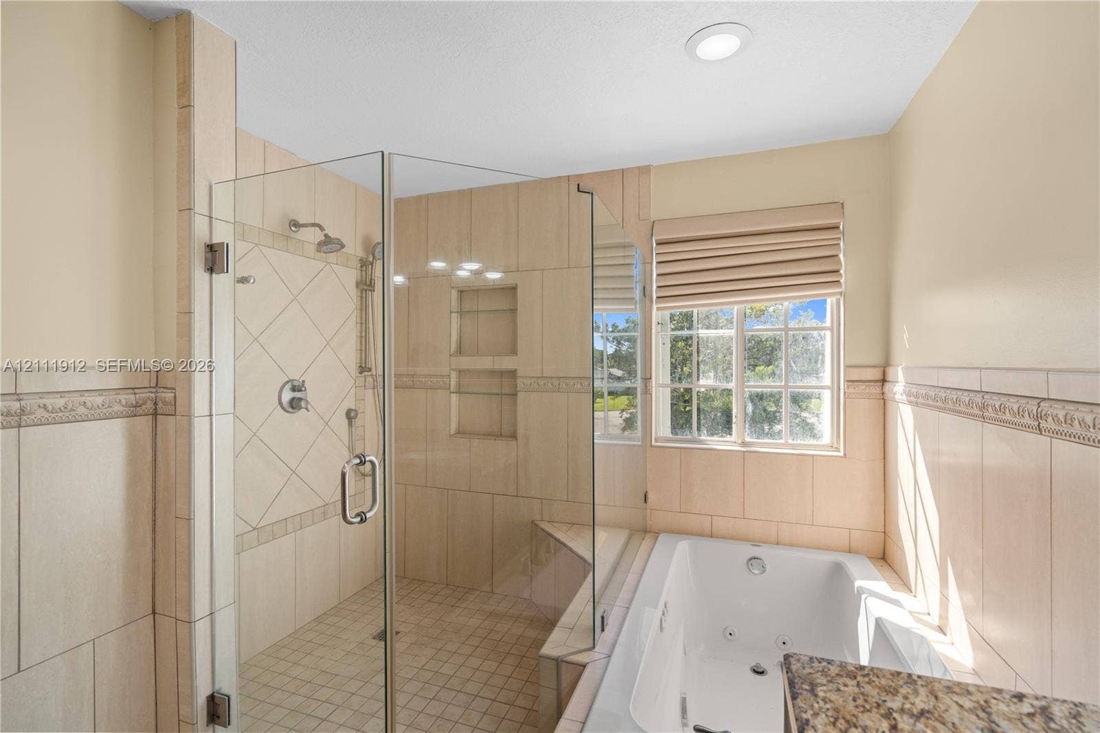 15681 SW 147th Court, Miami, FL 33187 Walk-in shower with glass enclosure, decorative tile surround, built-in shelving, jetted soaking tub, and window with pleated shade