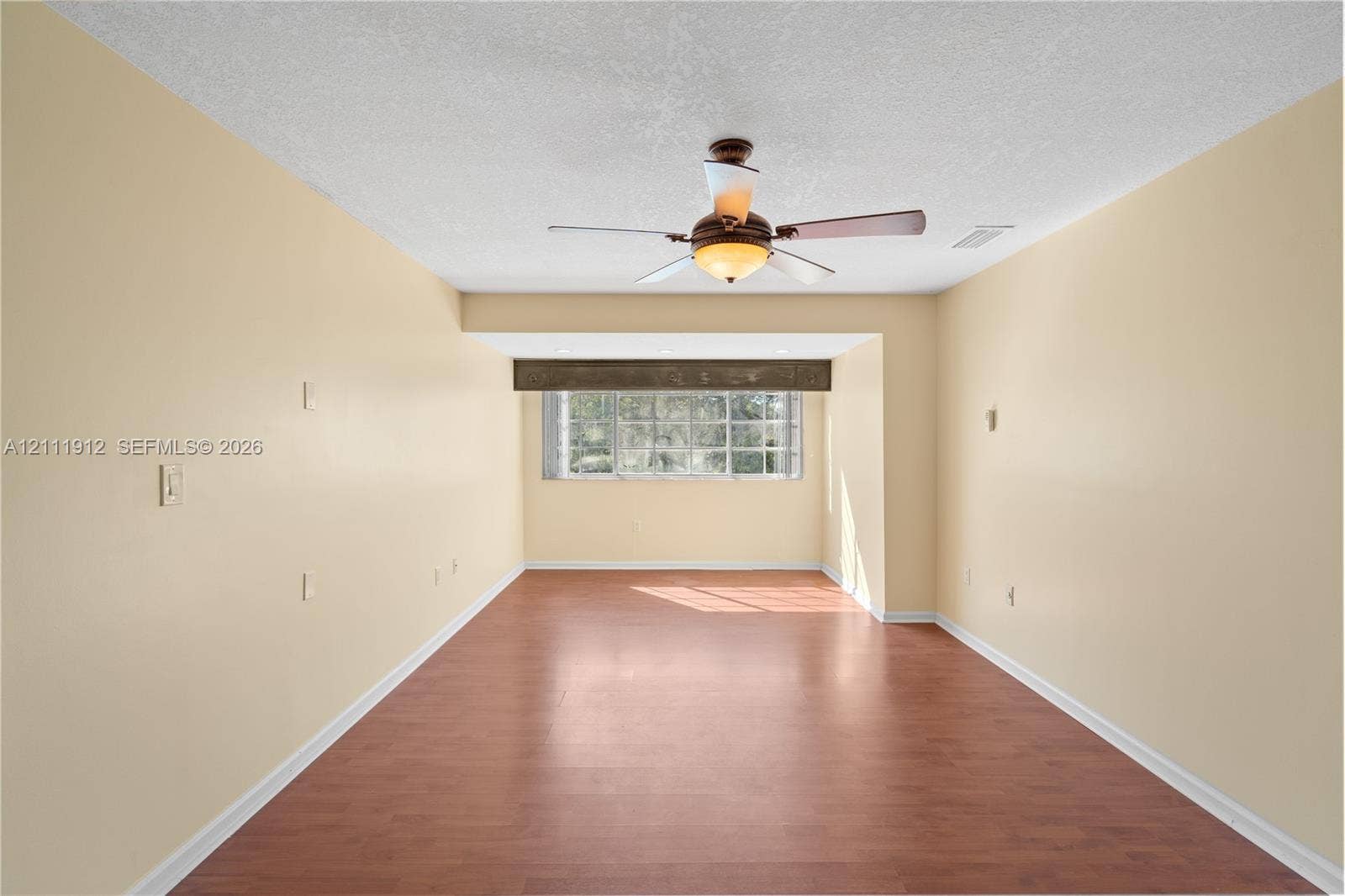 15681 SW 147th Court, Miami, FL 33187 Interior room featuring wood-finish flooring, a multi-pane window with a decorative valance, and a ceiling-mounted light fixture with integrated fan blades