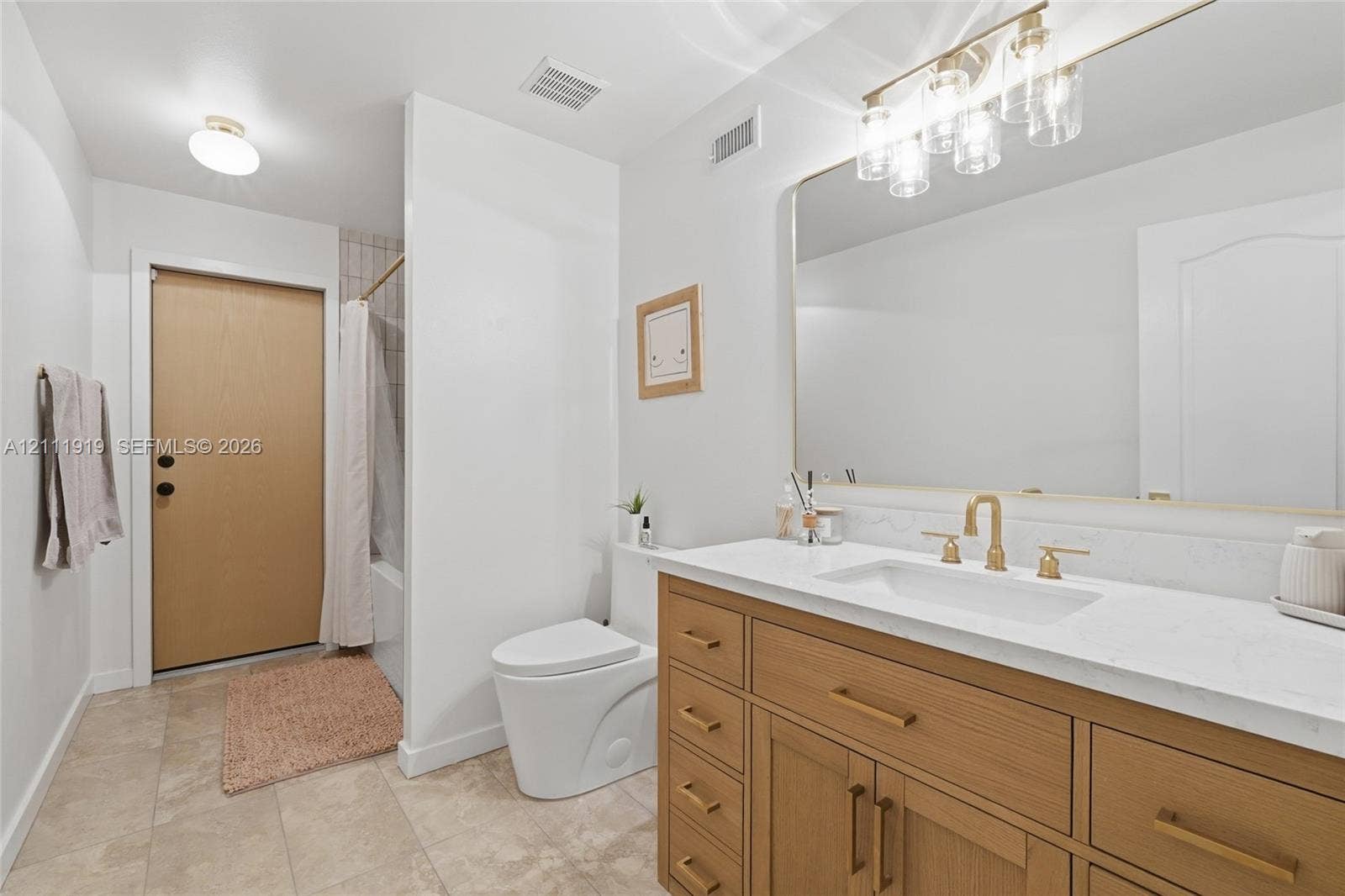 137 Arrowhead Lane, Haines City, FL 33844 Bathroom featuring a wood-finish vanity with a stone-surface countertop, rectangular undermount sink, brass-tone fixtures, oversized wall-to-wall mirror, and neutral tile flooring