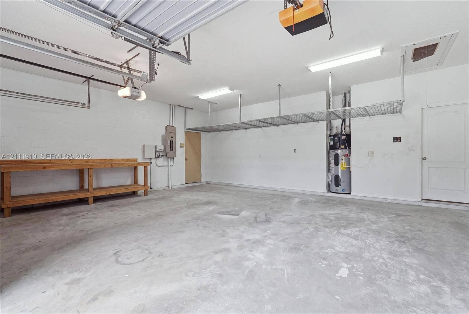 137 Arrowhead Lane, Haines City, FL 33844 Spacious garage featuring concrete flooring, built-in wooden workbench, overhead metal storage shelving, and dedicated water heater enclosure
