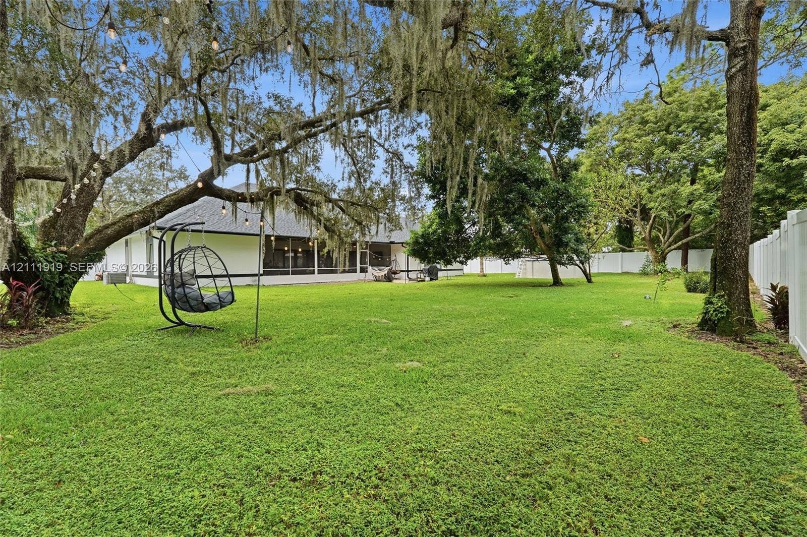 137 Arrowhead Lane, Haines City, FL 33844 Spacious backyard featuring a manicured lawn, mature trees, white privacy fencing, and a screened-in lanai