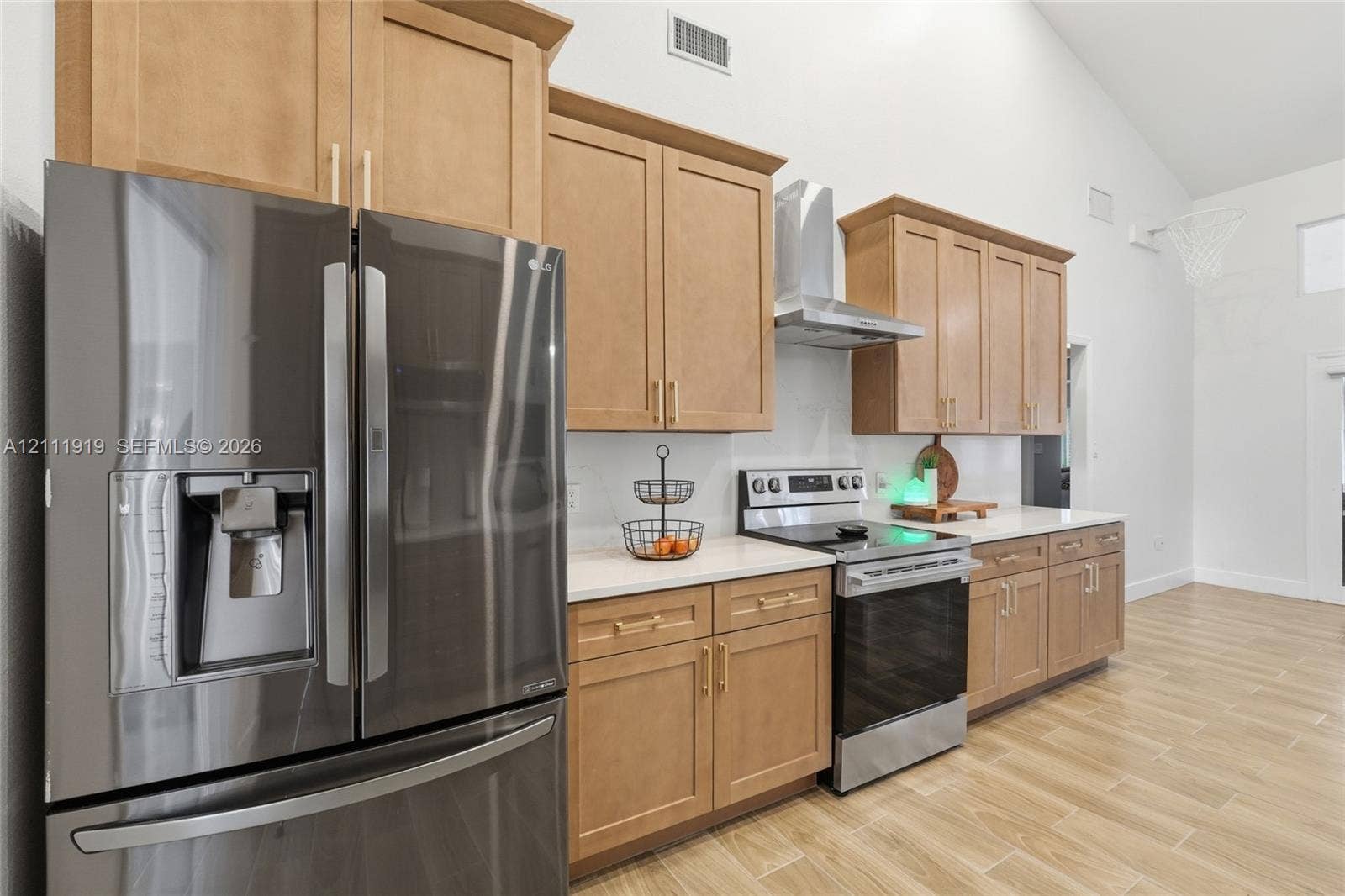 137 Arrowhead Lane, Haines City, FL 33844 Kitchen featuring wood-finish cabinetry, light-toned countertops, stainless steel appliances, a wall-mounted chimney-style range hood, and wood-finish flooring