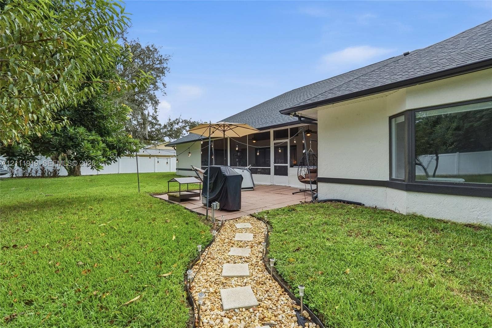 137 Arrowhead Lane, Haines City, FL 33844 Rear exterior featuring a screened-in lanai, concrete paver patio, gravel walkway with square stone steppers, and a white vinyl perimeter fence