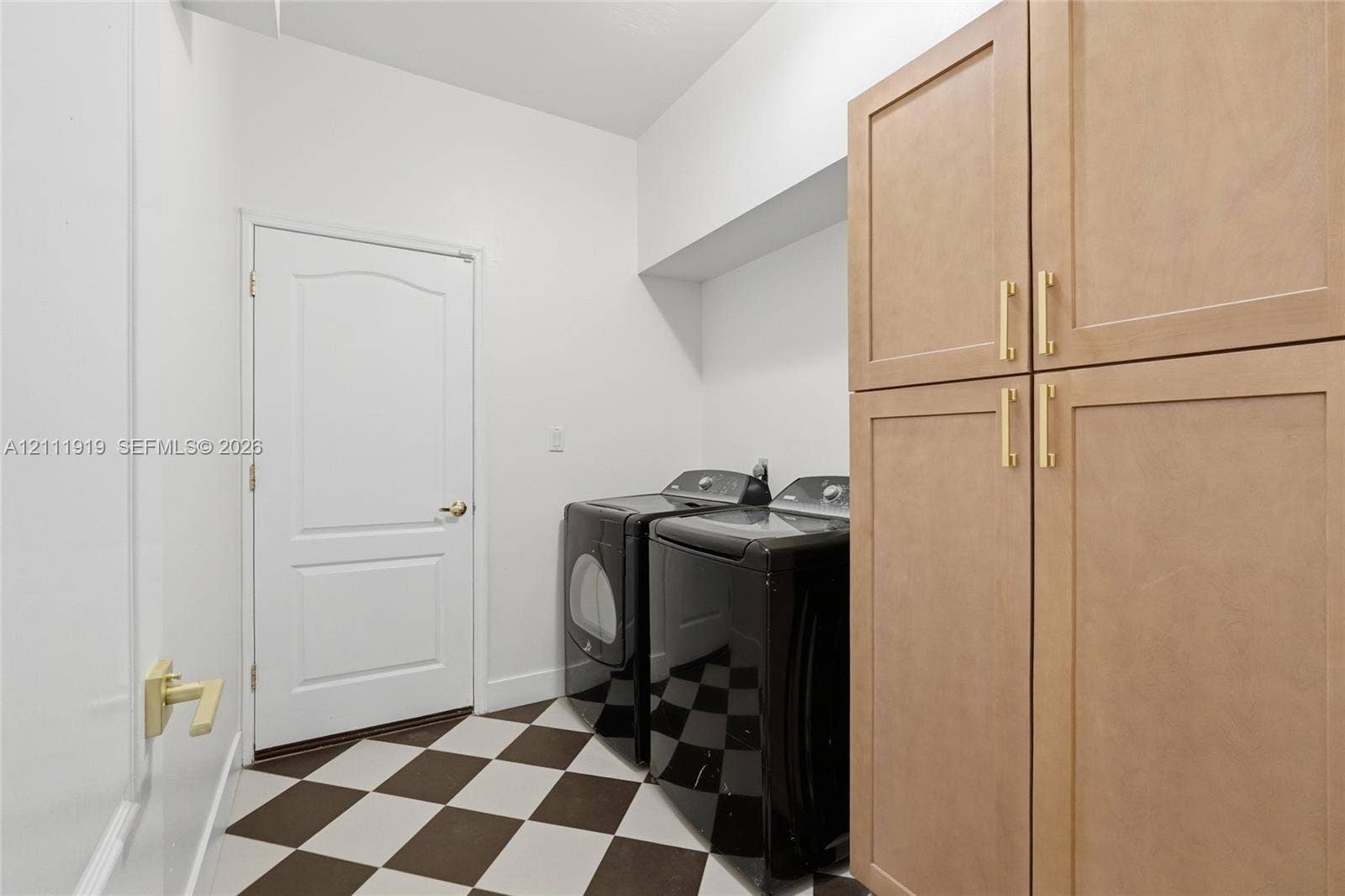 137 Arrowhead Lane, Haines City, FL 33844 Laundry area featuring built-in light wood cabinetry with gold-toned hardware, a checkerboard tile floor, and a solid-core door with a gold-toned lever handle