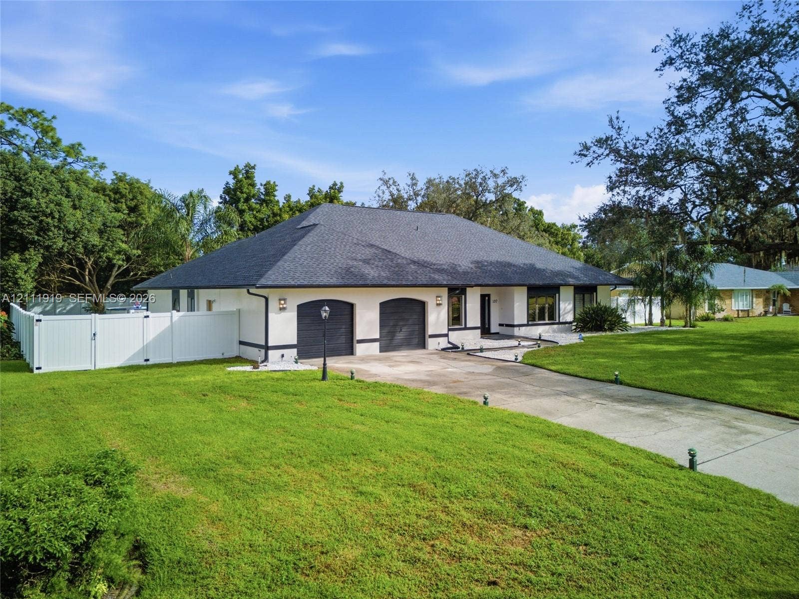 137 Arrowhead Lane, Haines City, FL 33844 Single-story exterior featuring a light-toned masonry facade, a hipped roof with dark shingles, two arched garage bays, and a surrounding privacy fence