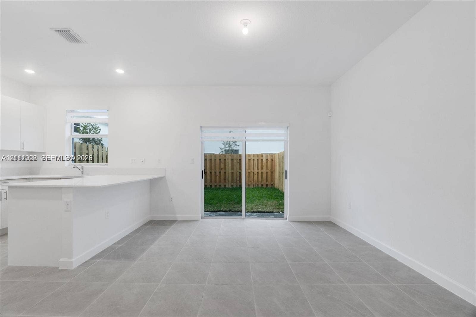 16281 SW 292nd Street, Homestead, FL 33033 Open-concept interior featuring large-format ceramic tile flooring, white cabinetry, quartz countertop kitchen peninsula, and sliding glass doors with direct access to the fenced backyard