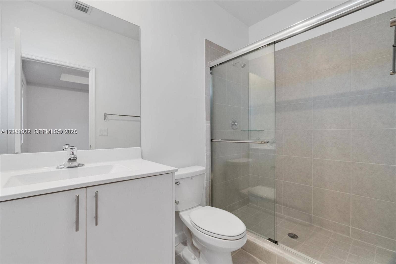 16281 SW 292nd Street, Homestead, FL 33033 Bathroom featuring a white vanity cabinet with a solid-surface countertop, an integrated sink with a chrome faucet, a large frameless mirror, and a walk-in shower with sliding glass doors and tiled wall surround