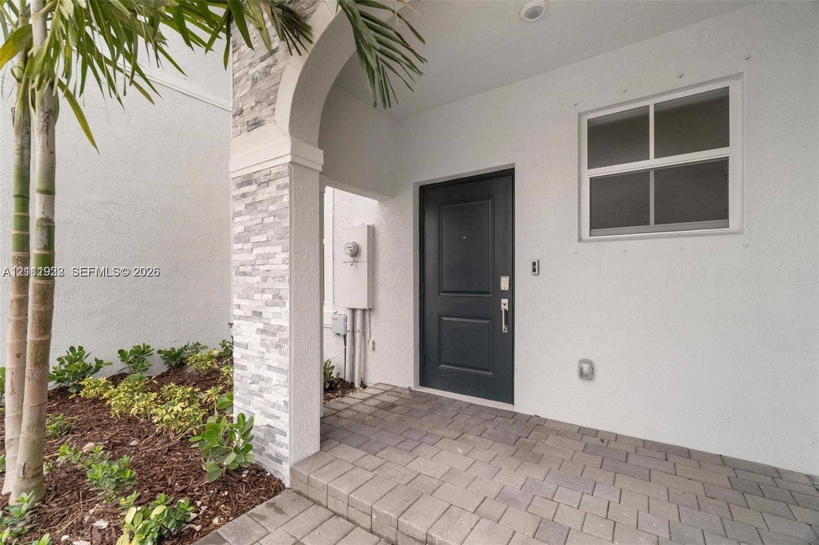 16281 SW 292nd Street, Homestead, FL 33033 Covered entryway featuring a stone-clad arched pillar, paved flooring, and a solid-panel front door